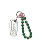 White Ford car key fob cover case, paired with a green beaded on pink wrist strap key chain, displayed on a white background.