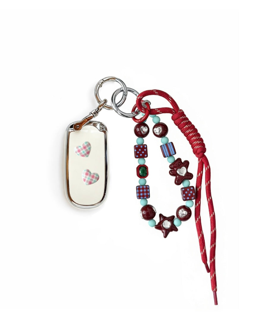 White Jeep car key fob cover case with pastel plaid heart design, paired with a handmade beaded keychain featuring cute patterned beads, and a red braided cord on a white background.