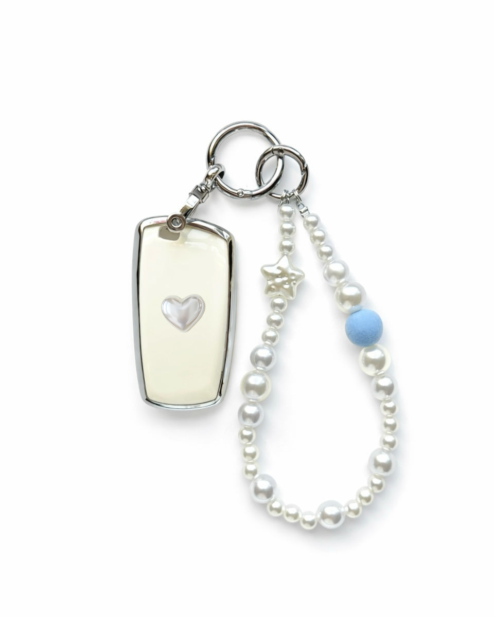 White Bmw key fob cover case with a pearl heart on the back, paired with a pearl white beaded wrist strap key chain featuring a blue accent bead and star charm, displayed on a white background.